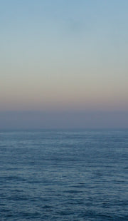 Twilight over the ocean. The water is still and a deep metalic cobalt. The sky is a subtle gradient from washed denim to faded purple.